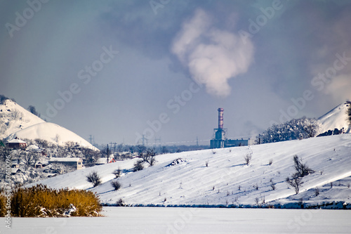 High and wide chimney, a pipe with a large amount of smoke and substances released into the atmosphere. Part of a factory or enterprise that pollutes the environment in a snowy and frosty winter near  © Анна Иванова