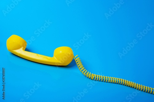 Yellow retro telephone receiver on blue background.