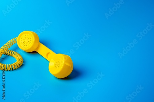 Yellow retro telephone receiver on blue background.