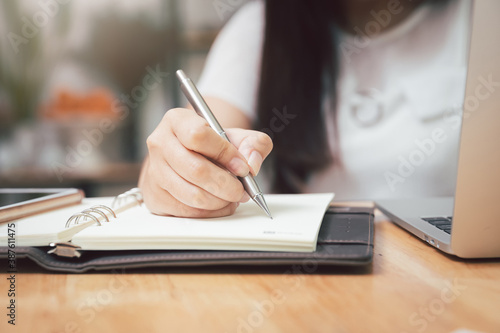 Closeup of woman's hand holding a pen on notebook. Freelance journalist working at home.