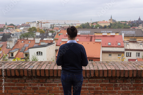 A girl watching a Prague landscape. She wears jeans, navy sweater and blue shirt.  photo