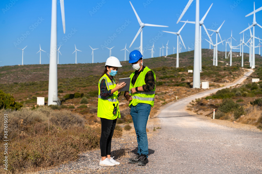 Technical businessman wearing protective face mask working in COVID-19 outbreak after novel coronavirus quarantine and lockdown standing with digital tablet pc on wind power energy station Technical businessman wearing protective face mask working in COVID-19 outbreak after novel coronavirus quarantine and lockdown standing with digital tablet pc on wind power energy station