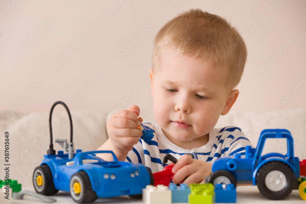 Toddler child plays with toy cars and colorful cubes on the table. Multi-colored plastic cubes for early child development. Early learning and educational toys for a little boy Toddler child plays with toy cars and colorful cubes on the table. Multi-colored plastic cubes for early child development. Early learning and educational toys for a little boy