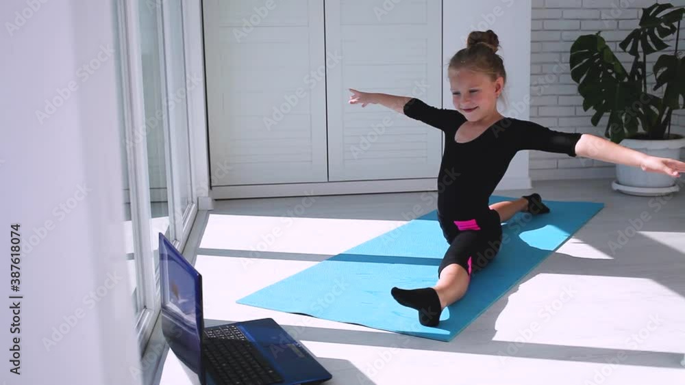 Fit little girl doing yoga plank and watching online lessons on laptop, exercising in the kitchen. A child plays sports during the COVID-19 pandemic. Fit little girl doing yoga plank and watching online lessons on laptop, exercising in the kitchen. A child plays sports during the COVID-19 pandemic.
