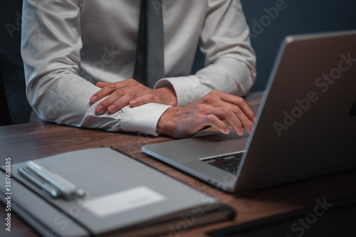 Businessman in white shirt and gray tie in front of a laptop on a wooden desk with items