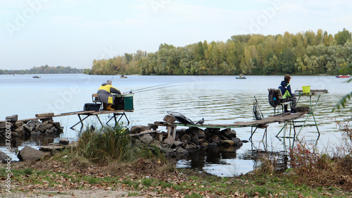 A fisherman catches fish on the river, rear view, from the bank. A fisherman sits on a wooden and stone bridge on the river bank and tries to catch fish. Sports, recreation, lifestyle