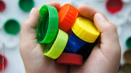 Childs hands holding colourful plastic bottles caps for recycling to conserve the environment. White background. Heart in hands.Recycling and protection Earth concept.