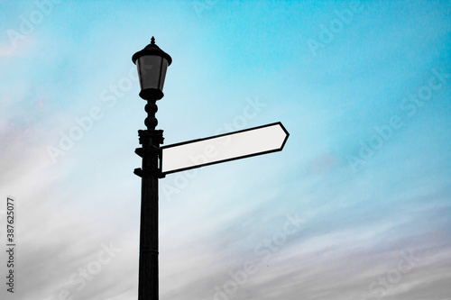 Object photograph of an isolated vintage street lamp with one blank white direction indicator on it against blue sky