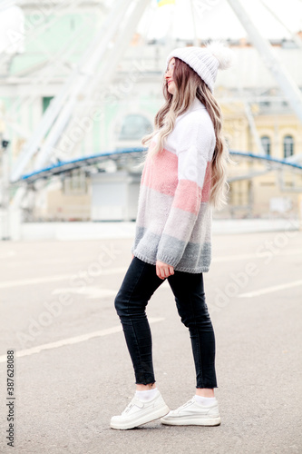 Outdoors lifestyle fashion portrait of stunning blonde young woman. Wearing stylish pullover, knitted hat.