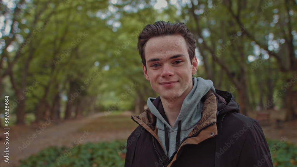 Young happy man looks to the camera. Happy smiling male face, outdoors. Close up of Teenager's face. Slowly zooming to the human's face.a teenage boy stands in the park and enjoys life. look straight Young happy man looks to the camera. Happy smiling male face, outdoors. Close up of Teenager's face. Slowly zooming to the human's face.a teenage boy stands in the park and enjoys life. look straight