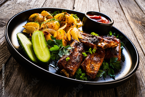 Tasty roasted ribs with baked potatoes vegetables on wooden table 