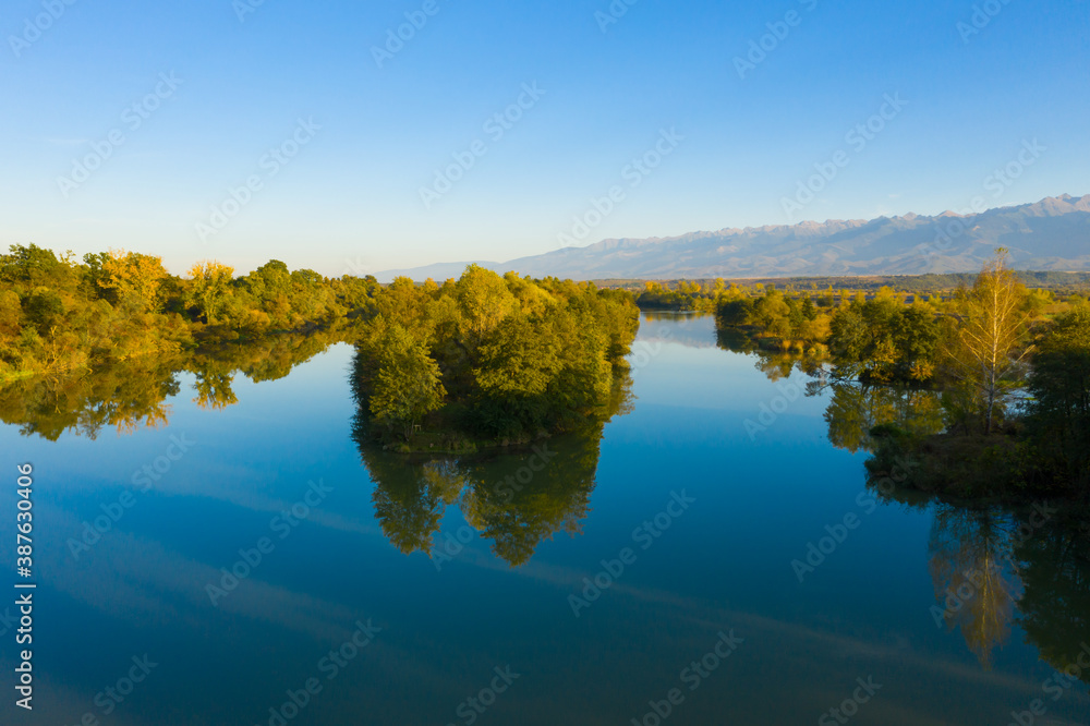 Lake at the edge of the mountains with forest reflected in the clear water. Idyllic autumn landscape. The forest and the sky in the reflection of the water. Quiet autumn fishing landscape