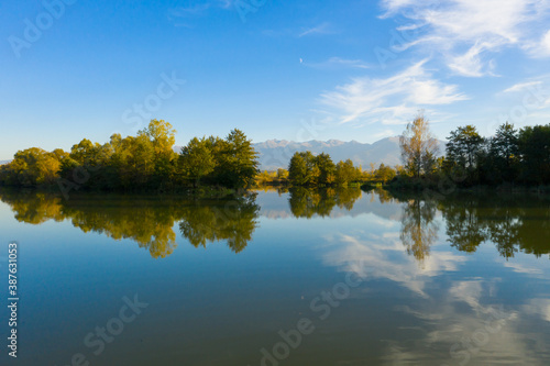 Lake at the edge of the mountains with forest reflected in the clear water. Idyllic autumn landscape. The forest and the sky in the reflection of the water. Quiet autumn fishing landscape
