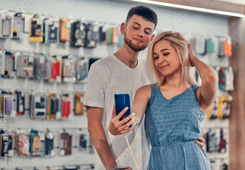 Close up focus view of a stylish charming embracing young student love couple taking a selfie with new mobile in a tech store.