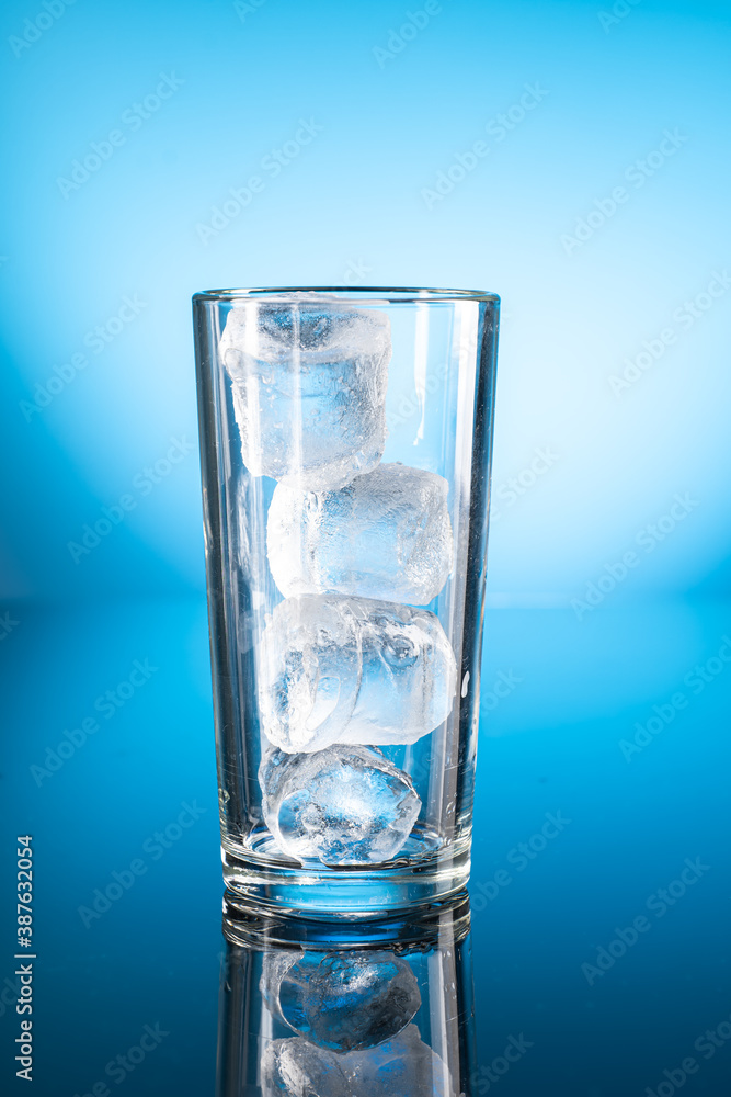 Clear ice water in transparent glass with reflection on blue gradient background Clear ice water in transparent glass with reflection on blue gradient background