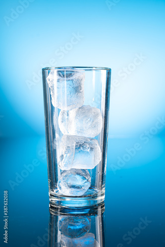 Clear ice water in transparent glass with reflection on blue gradient background