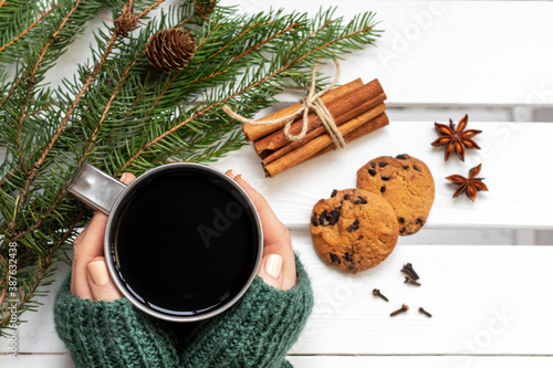 Female hands holding metal mug with hot coffee at white wooden table. Christmas hot drink. Copy space, top view.