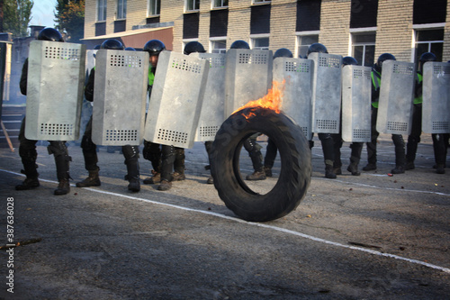 a group of policemen with shields disperses a protest against the background of a burning tire. Tactical training