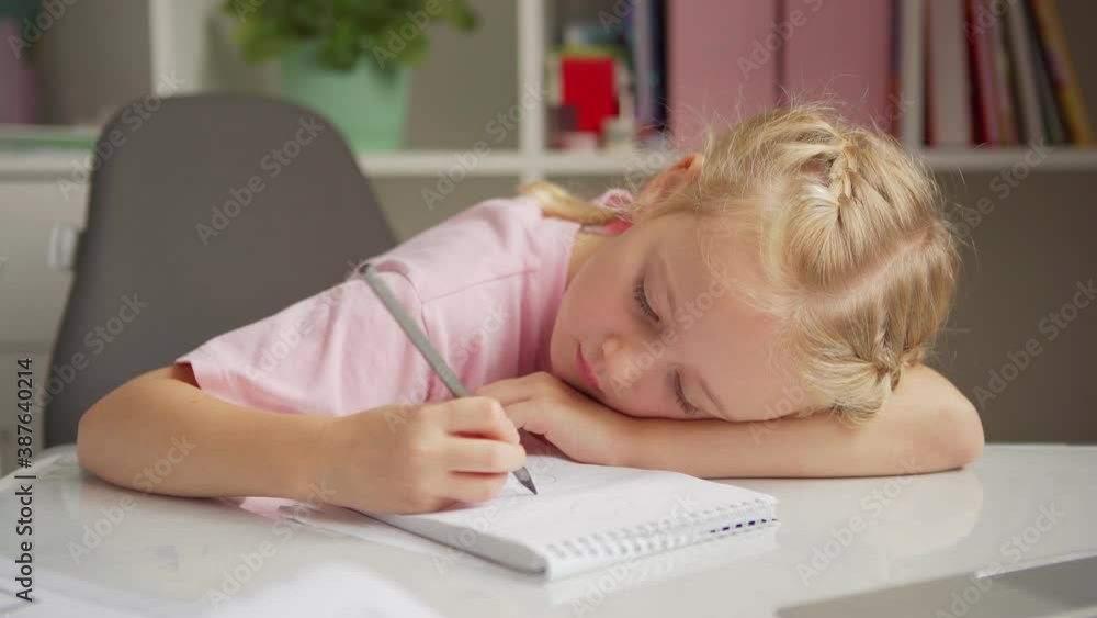 Tired elementary school girl lying down on desk and drawing hearts in her notepad while doing homework at home Tired elementary school girl lying down on desk and drawing hearts in her notepad while doing homework at home