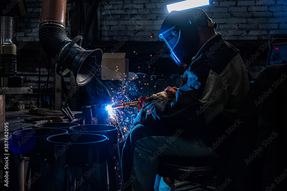 Side view of welder in protective helmet welding metal detail with sparks at factory Side view of welder in protective helmet welding metal detail with sparks at factory