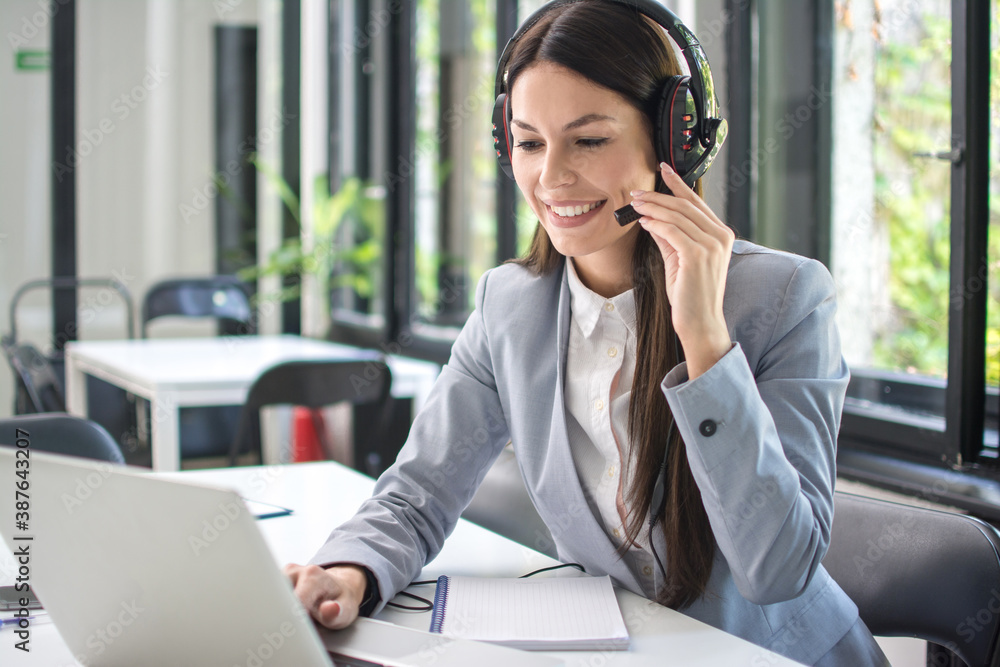Smiling business woman with headset using laptop in office