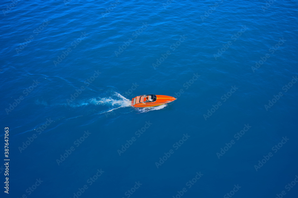 Side view of the speed boat. A large, orange speedboat moving on blue water. Aerial view of fast boat movement. Lonely boat, movement on the water.