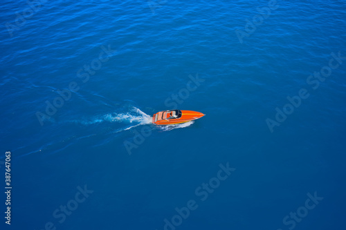 Side view of the speed boat. A large, orange speedboat moving on blue water. Aerial view of fast boat movement. Lonely boat, movement on the water.