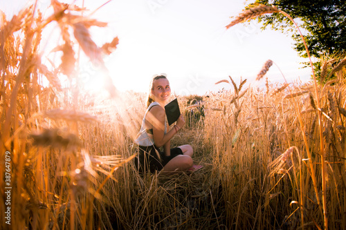 Young brunetter sitting a wheat field holding a book during a golden sunset - creativity, freedom concept photo