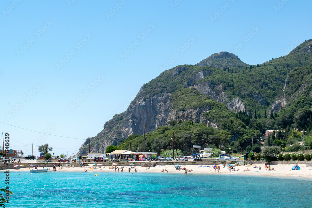 Agios Spiridon beach in Palaiokastritsa, Corfu, Greece with the nearby cliffs towering over it