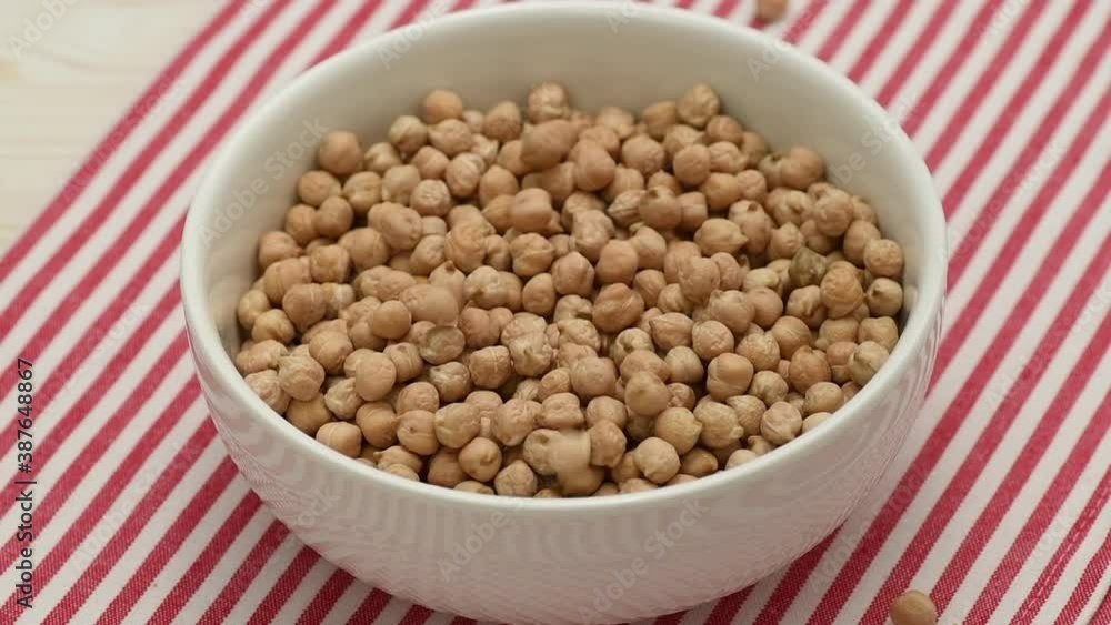Dry raw chickpeas falling into a white bowl, slow motion, close up Dry raw chickpeas falling into a white bowl, slow motion, close up