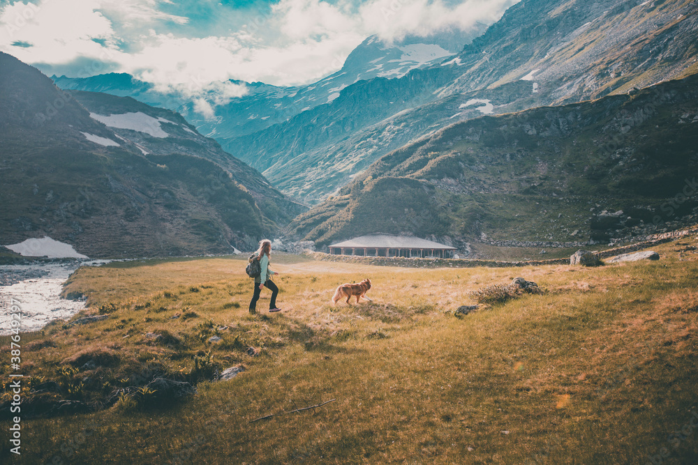 Young blond woman walking with her border collie dog in wild, austrian mountains in a national park - freedom, travel, hiking, exploring