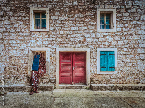 Close up view of old stone house, red wooden door and blue windows. Prvic luka, Summer in Croatia.