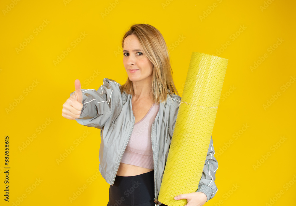 Beautiful woman holding yoga mat in hand over yellow background. Beautiful woman holding yoga mat in hand over yellow background.