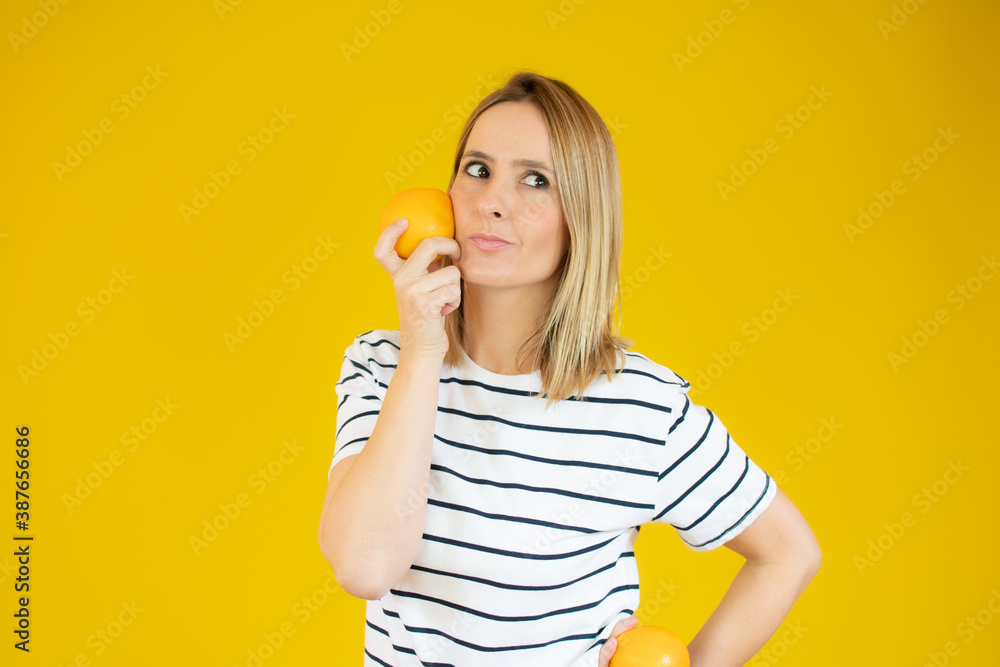 Woman in a striped white T-shirt with an orange in her hand on a yellow background Woman in a striped white T-shirt with an orange in her hand on a yellow background
