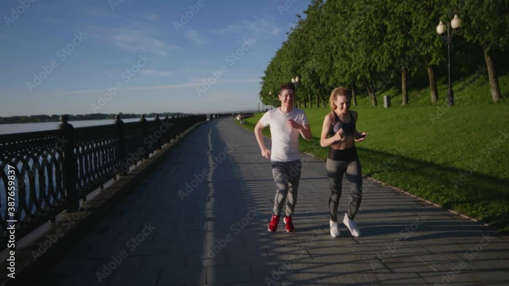 Guys in sportswear running or jogging on embankment or waterfront of river in early morning after waking up. Brunette guy and blonde girl preparing together for marathon. Concept of healthy lifestyle. Guys in sportswear running or jogging on embankment or waterfront of river in early morning after waking up. Brunette guy and blonde girl preparing together for marathon. Concept of healthy lifestyle.