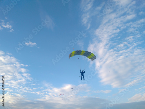 A skydiver with a bright orange sports parachute wing flies before landing in the summer against a blue sky background close up