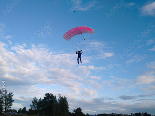 A skydiver with a bright orange sports parachute wing flies before landing in the summer against a blue sky background close up