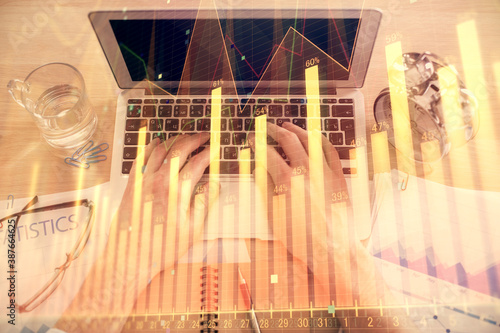 Double exposure of man's hands typing over laptop keyboard and forex chart hologram drawing. Top view. Financial markets concept.