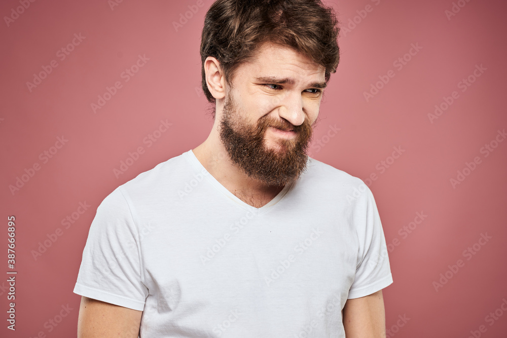 Fototapeta premium Emotional bearded man in white T-shirt discontent pink background