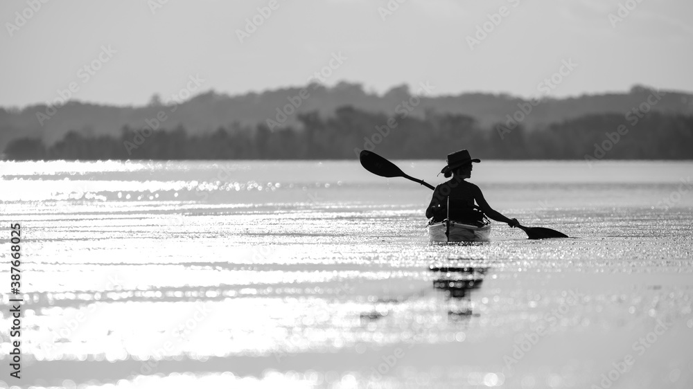 Silhouette of a woman paddling her kayak at sunset.
