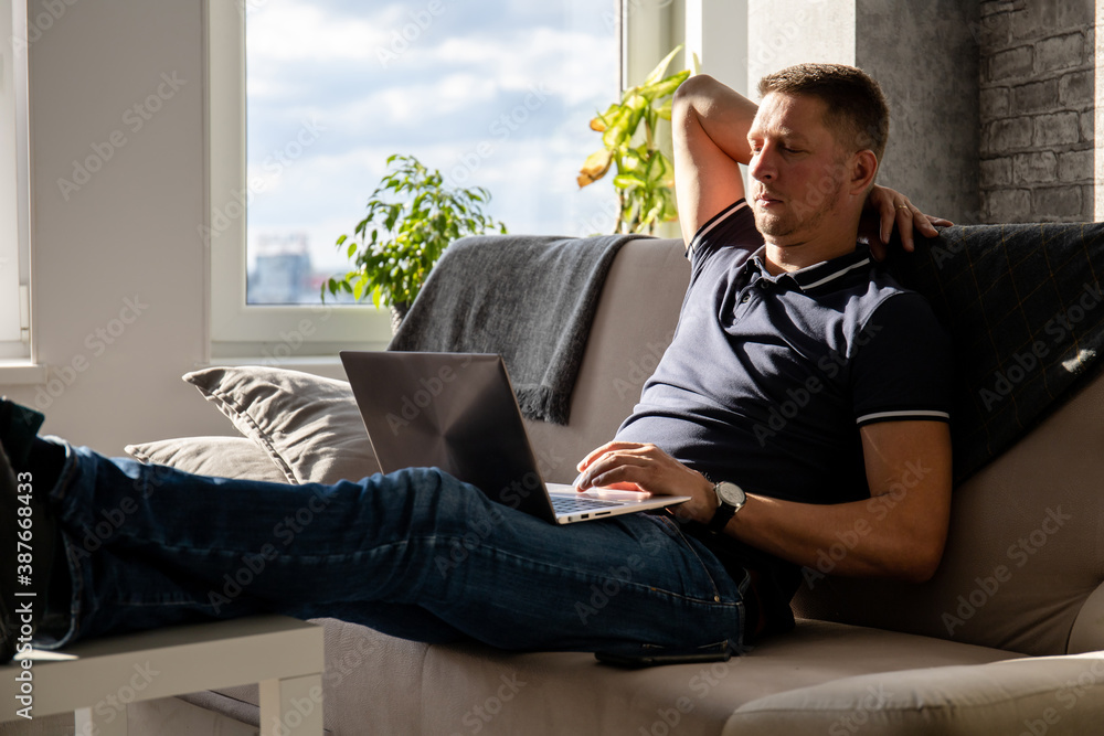 middle aged man resting on sofa with laptop on his legs