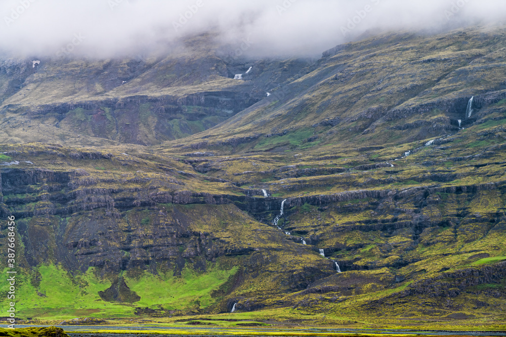Iceland mountain landscape view of cliff and waterfall river on cloudy day on south southern ring road in summer near fjadrargljufur