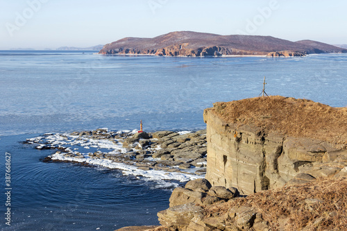 The rocky coast of Cape Tobizin on the Russian Island in Vladivostok, covered with snow and floating ice, on a sunny winter day. photo