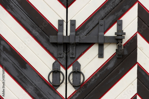 Obraz na plátně Wrought iron door handles in the form of a ring and a steel bolt closed with a padlock on the gate in a medieval castle