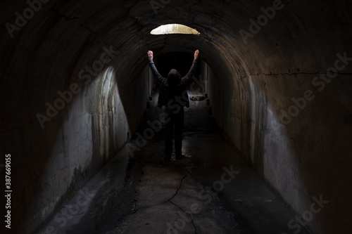 A man in a dark underground tunnel is looking for a way out and raises his hands to the sky asking for help. © Сергей Рамильцев