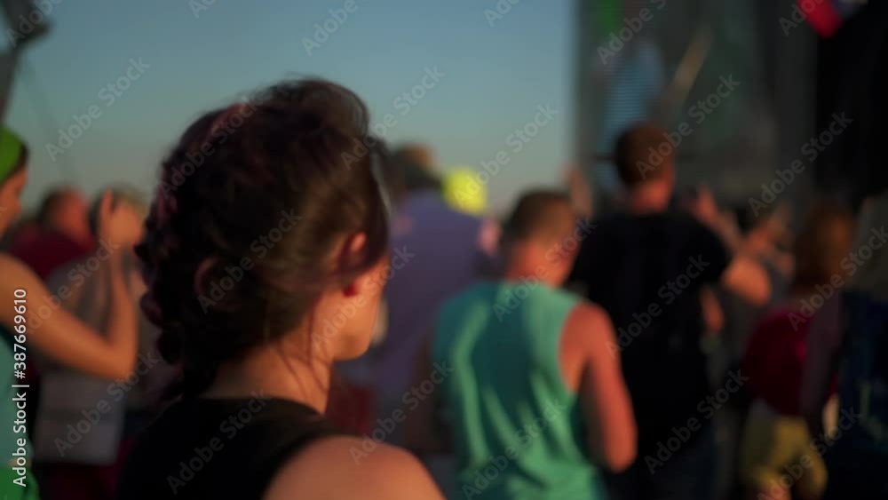 Rear view of asian woman dancing among the crowd of people at rock concert festival. Music fans enjoying summer gig. Concept of youth culture and entertainment.