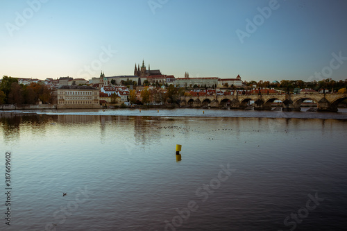 view of the Vltava river and Prague Castle St. Vitus Cathedral and Charles Bridge in the center of Prague at sunset. there are reflections on the river surface and the sky is illuminated by the sun