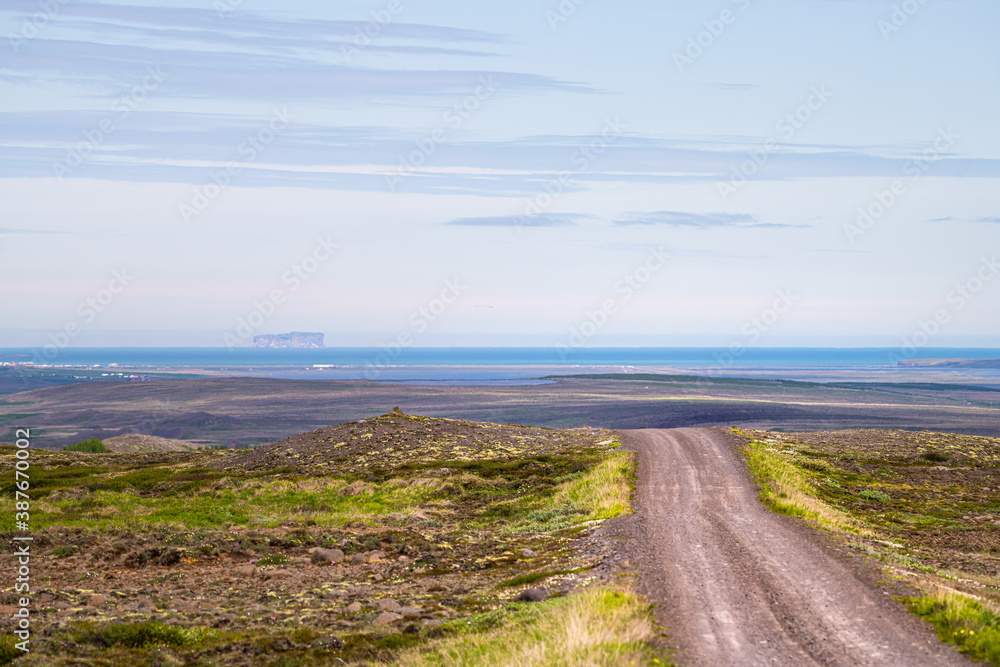 View of Blonduos cityscape west of Akureyri with blue sky during summer day and dirt road leading to ocean and water in horizon in Iceland