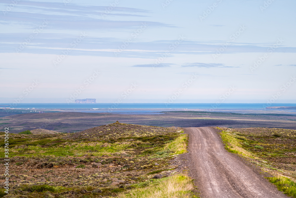 View of Blonduos cityscape west of Akureyri with blue sky during summer day and dirt road leading to ocean and water in horizon in Iceland View of Blonduos cityscape west of Akureyri with blue sky during summer day and dirt road leading to ocean and water in horizon in Iceland