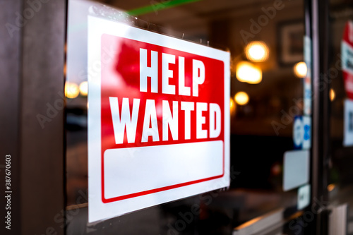 Sign text closeup for help wanted with red and white colors by entrance to store shop business building during corona virus covid 19 pandemic © Andriy Blokhin